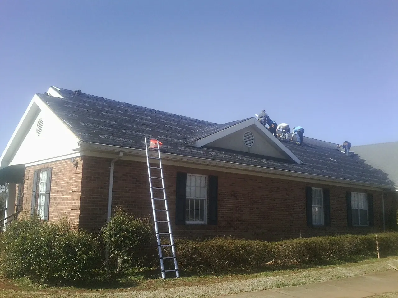 Crew tearing shingles off a brick ranch roof with a ladder set — Emergency Roof Repair work by our crew in Eagle