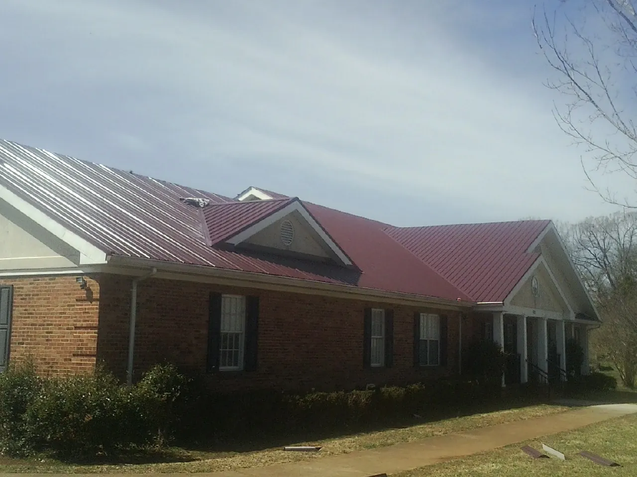Red metal roof with gabled entries on a long brick building, from a Hail Damage Roof Repair job in Eagle