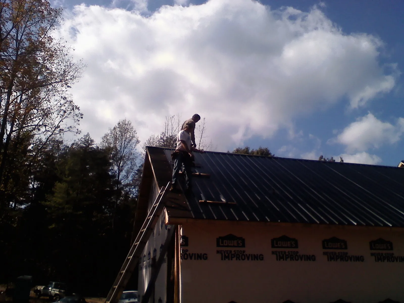 Roofer fastening dark metal panels high against a cloudy sky, from a Roof Inspection job in Eagle